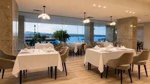 A restaurant with tables set for dining, large windows offering a view of the water, and modern lighting fixtures. - Obelisk Nile Towers (Aswan)