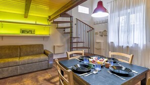 A dining area with a table set for four, a sofa, a staircase, and a pendant light. - Casa Il Maestro by Rentbeat (Civitavecchia)