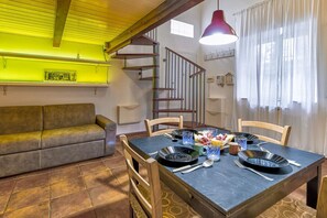 A dining area with a table set for four, a sofa, a staircase, and a pendant light.