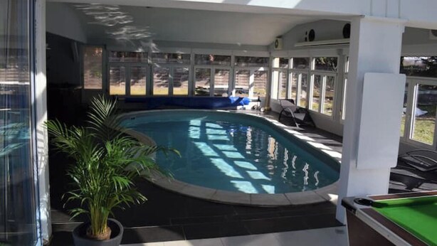 En pool med tak som skyddar mot väder och vind, med utsikt över trädgården, en krukväxt och ett biljardbord.