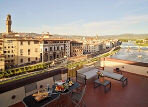 Una terraza con mesa lista para comer, con vistas a un río y edificios históricos.