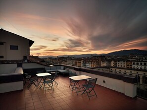 Terraza en la azotea con asientos exteriores, vistas panorámicas de la ciudad y un cielo al atardecer.