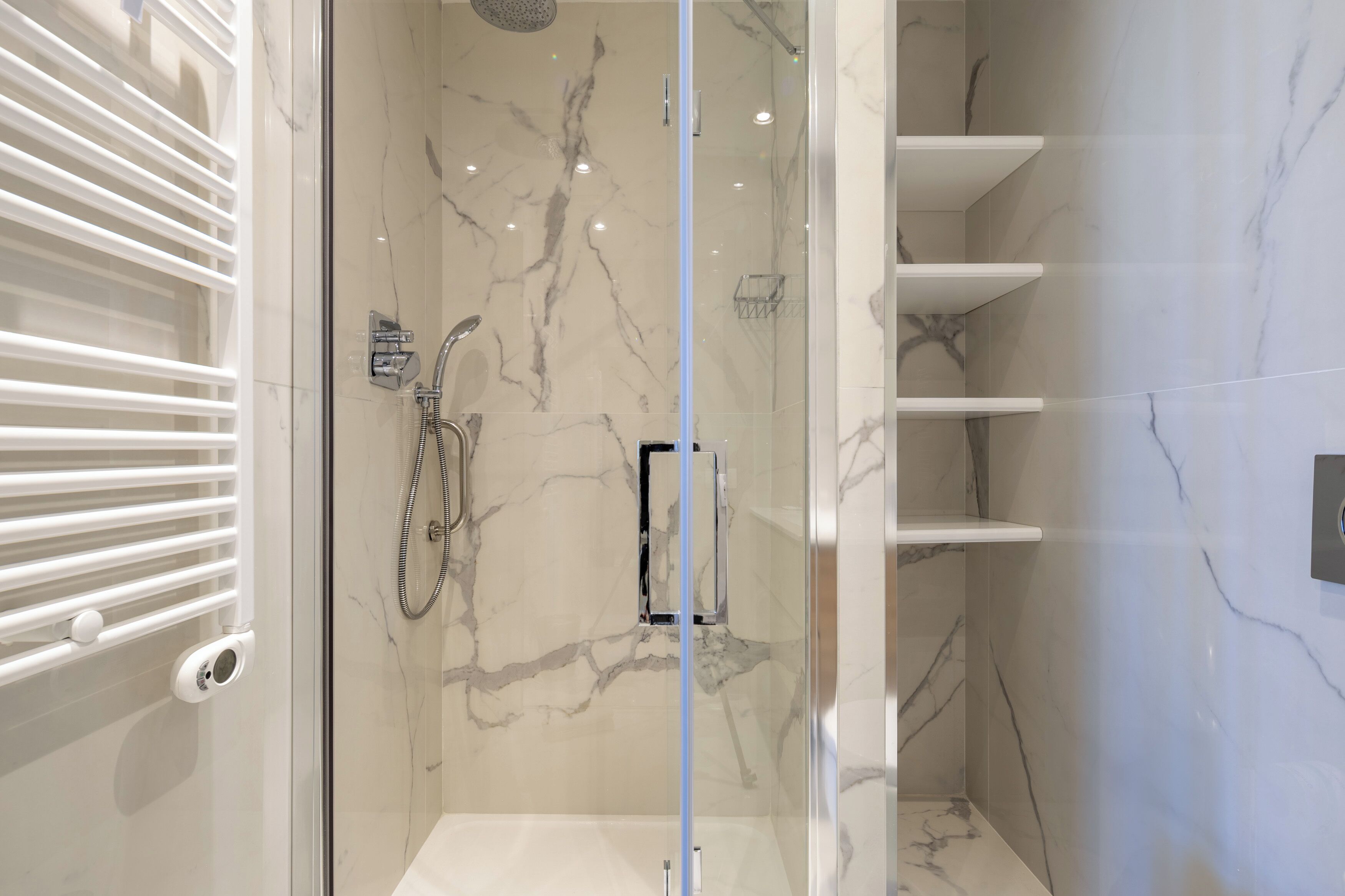 A modern bathroom with a glass-enclosed shower, marble walls, and built-in shelves.