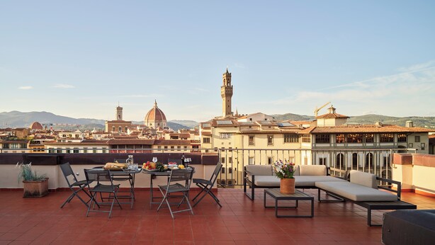 A rooftop terrace with a table set for dining, outdoor seating, and a view of historic buildings and mountains. - Luxury Apartment and Terraces - Medici Penthouse (Firenze)