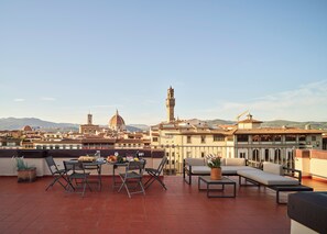 A rooftop terrace with a table set for dining, outdoor seating, and a view of historic buildings and mountains.