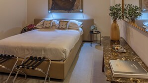 A bedroom with a wooden ceiling, a bed with white bedding, a small bedside table with a lamp, a mirror, and a plant. - Luxury Apartment and Terraces - Medici Penthouse (Firenze)