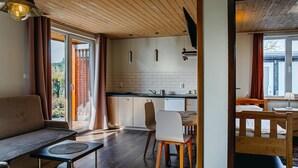 A modern living room with a sofa, a dining table, and chairs. There is a kitchen area with cabinets and a window. - Ground Floor Holiday Studio, Gaski (Mielno)