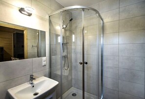 Ett modernt badrum med en dusch som är avskärmad med glasväggar, ett handfat och en spegel.