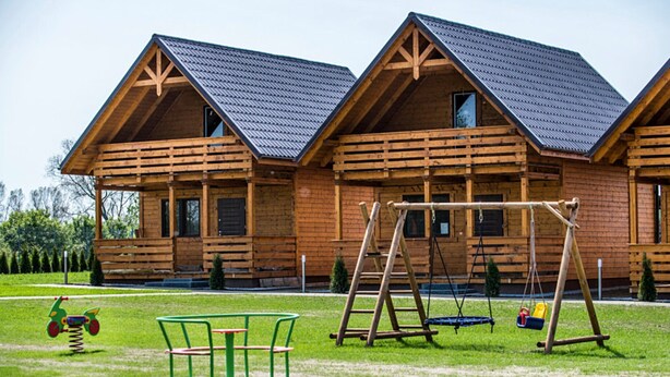 A wooden cabin with a porch, a swing set, and a children's play area. - Two-storey Holiday Cottages, Plesna (gmina Bedzino)