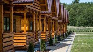 A row of wooden cabins with sloped roofs, arranged in a linear fashion along a paved pathway. - Two-storey Holiday Cottages, Plesna (gmina Bedzino)