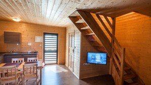 A wooden cabin interior with a dining area, kitchen, and a TV mounted on the wall. - Two-storey Holiday Cottages, Plesna (gmina Bedzino)