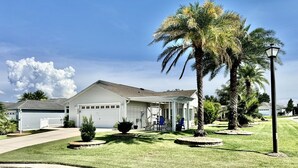 A single-story house with a garage, surrounded by well-maintained lawns and palm trees. - Sunscape Palms - 3/2 with Golf Cart & Grill in The Village of St. James (St. James, The Villages)