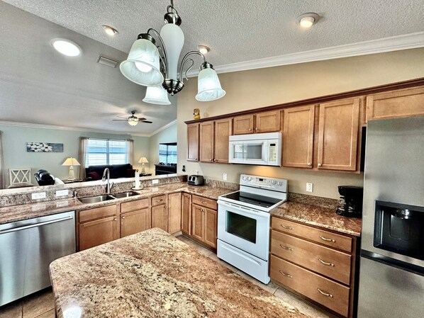 A modern kitchen with granite countertops, stainless steel appliances, wooden cabinets, and a central island.