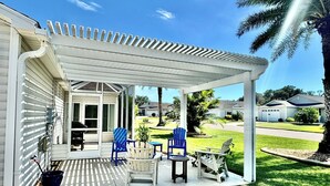 A covered patio with outdoor furniture, a grill, and a view of a residential neighborhood. - Sunscape Palms - 3/2 with Golf Cart & Grill in The Village of St. James (St. James, The Villages)