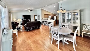 A spacious living room with a fireplace, a dining area with a round table, and a kitchen with wooden cabinets. - Sunscape Palms - 3/2 with Golf Cart & Grill in The Village of St. James (St. James, The Villages)