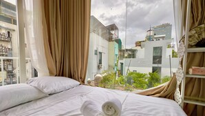 A hotel room with a bed, curtains, and a view of the cityscape. - Cherry Blossom Boutique Hotel (Ho Chi Minh City)