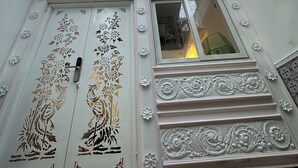 A building with ornate white doors featuring floral and bird designs, a window with a view of the interior, and a balcony with decorative railings. - Cherry Blossom Boutique Hotel (Ho Chi Minh City)