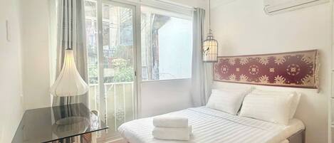 A bedroom with a bed, a desk, a chair, and a window with curtains.