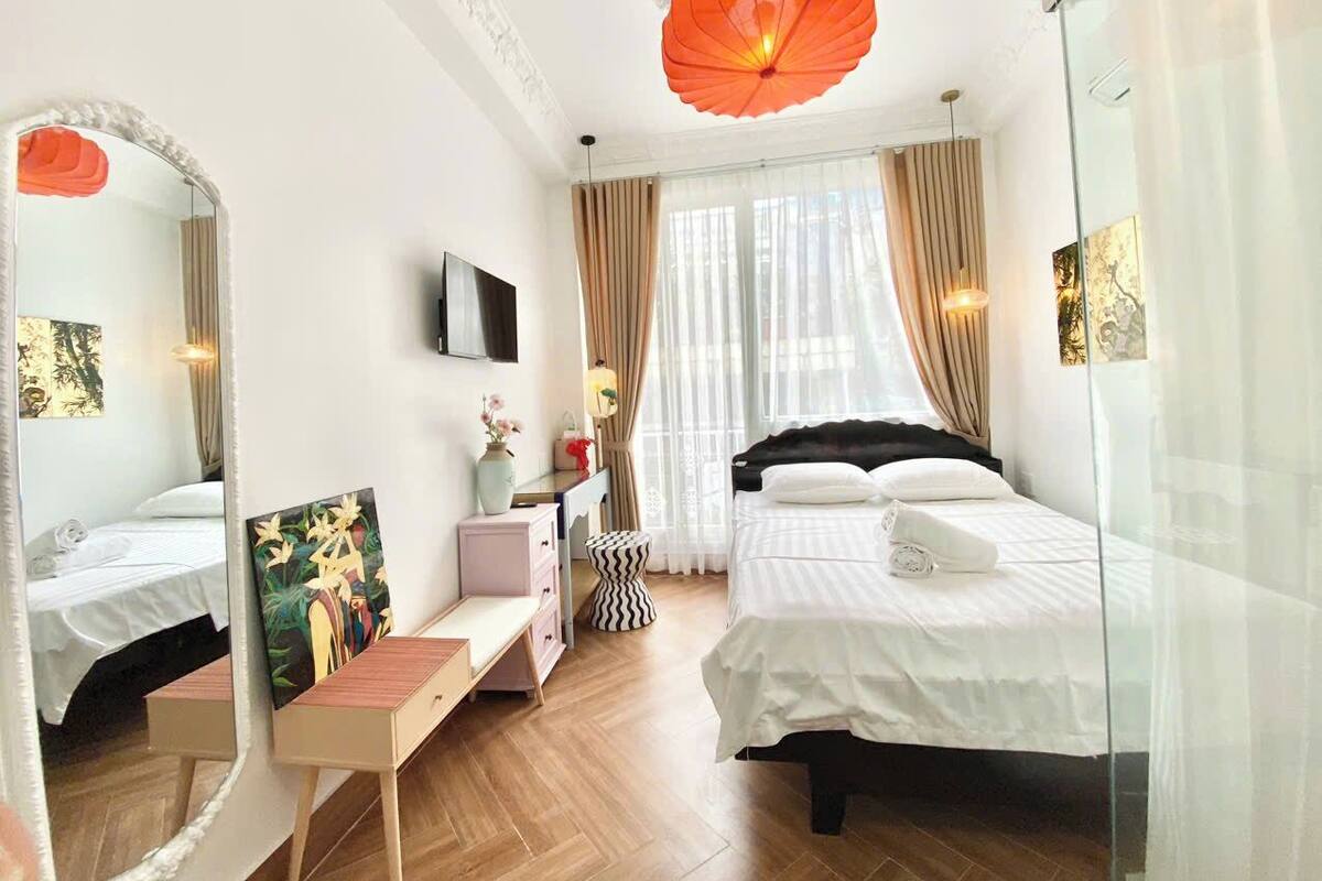 A hotel room with a bed, a desk, a chair, a TV, and a large mirror.