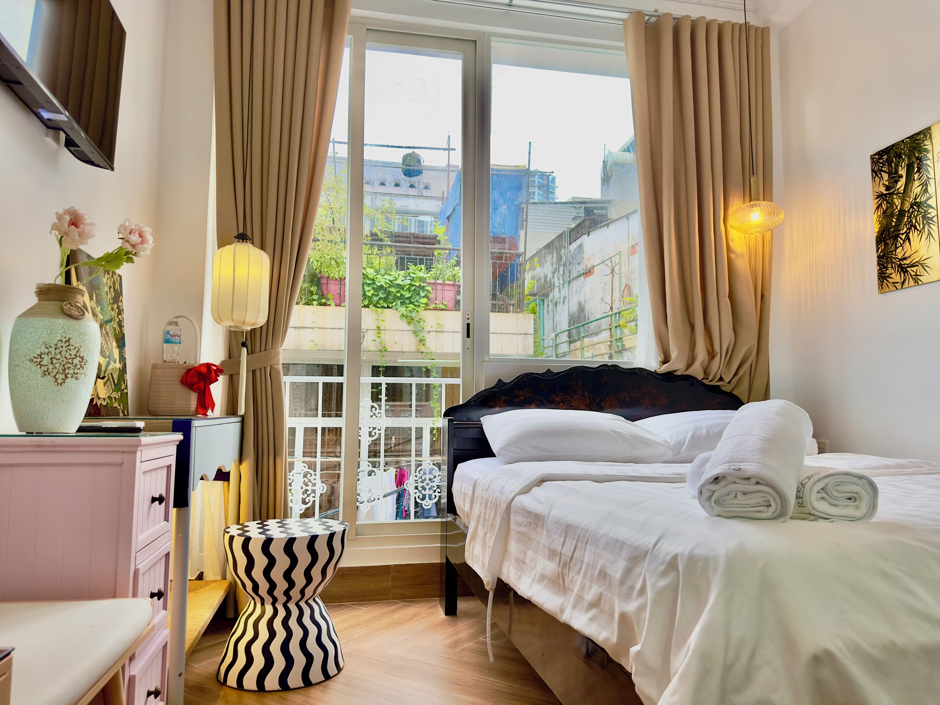 Habitación de hotel con cama, mesita de noche, lámpara y vistas al exterior.