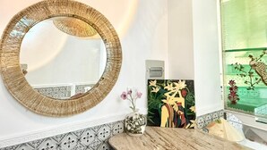 A round mirror with a textured frame on a wall, a vase with flowers, and a framed artwork with floral and abstract designs. - Cherry Blossom Boutique Hotel (Ho Chi Minh City)