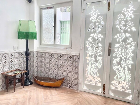 A room with patterned tile walls, a wooden boat, a table, a lamp, and a door with floral cut-out designs. - Cherry Blossom Boutique Hotel (Ho Chi Minh City)