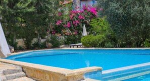 A swimming pool with a stone edge, surrounded by lush greenery and a pink flowering tree. - Villa Lycia with Sea Platform (Kas)