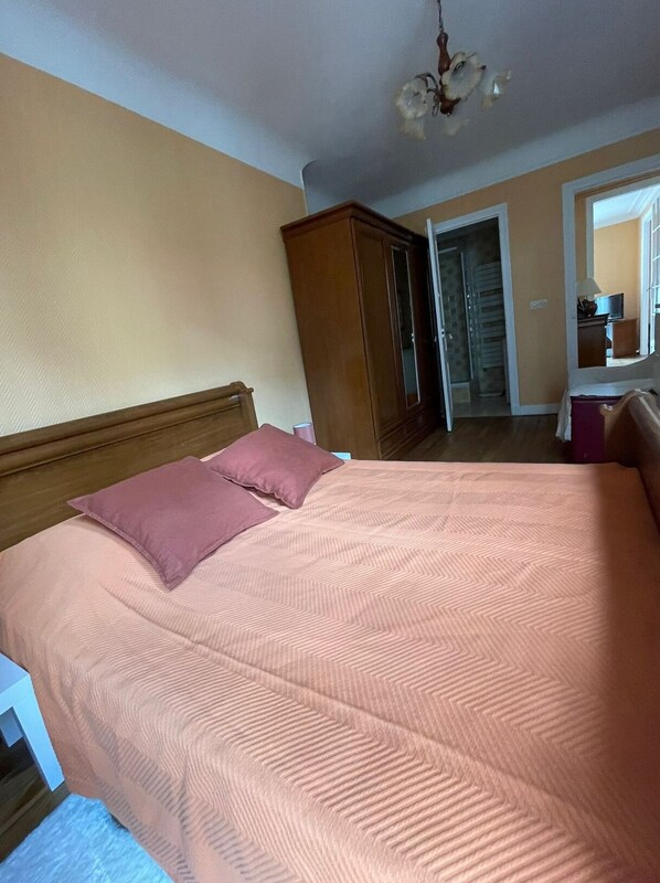 Een slaapkamer met een bed, een houten kledingkast en een deur naar een andere kamer.