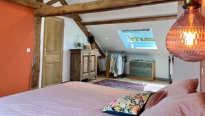 A bedroom with a sloped ceiling, wooden beams, a skylight, a bed with pink bedding, a dresser, and a hanging light fixture.