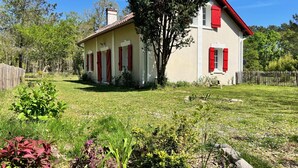 A two-story house with a red roof and white walls, surrounded by a well-maintained garden and a wooden fence.