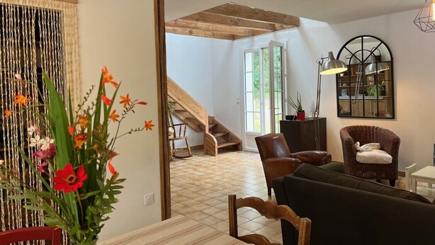 A spacious living area with a staircase leading to an upper floor, a dining table with chairs, and a large mirror on the wall.