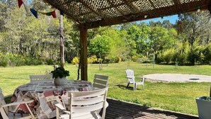 A wooden deck with a table and chairs, surrounded by a grassy area and trees.