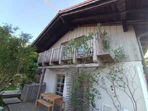 Un edificio de madera con balcón, una mesa de madera y un pequeño jardín.