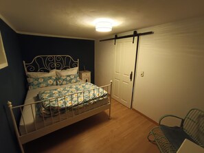 Un dormitorio con estructura de cama metálica, suelo de madera, una puerta blanca y una mesita de noche pequeña.