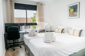 A hotel room with two beds, a desk, a chair, and a window with curtains.