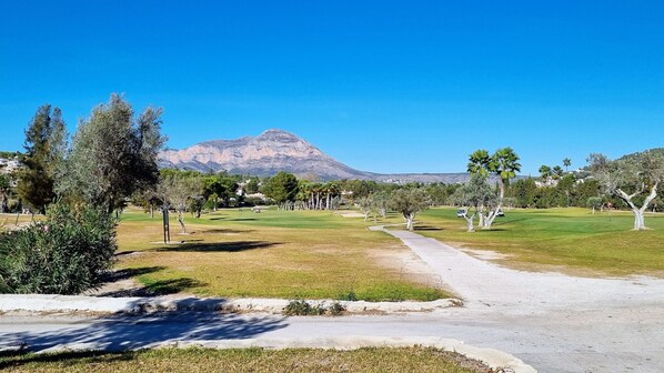 A golf course with a mountain in the background, trees, and a clear sky.