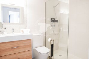 A modern bathroom with a glass-enclosed shower, a white toilet, a wooden vanity with a mirror, and a white sink.