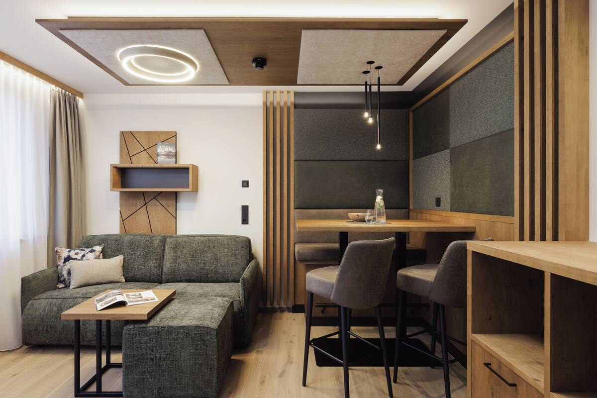 A modern living room with a sectional sofa, a wooden coffee table, and a dining area with a wooden table and bar stools.