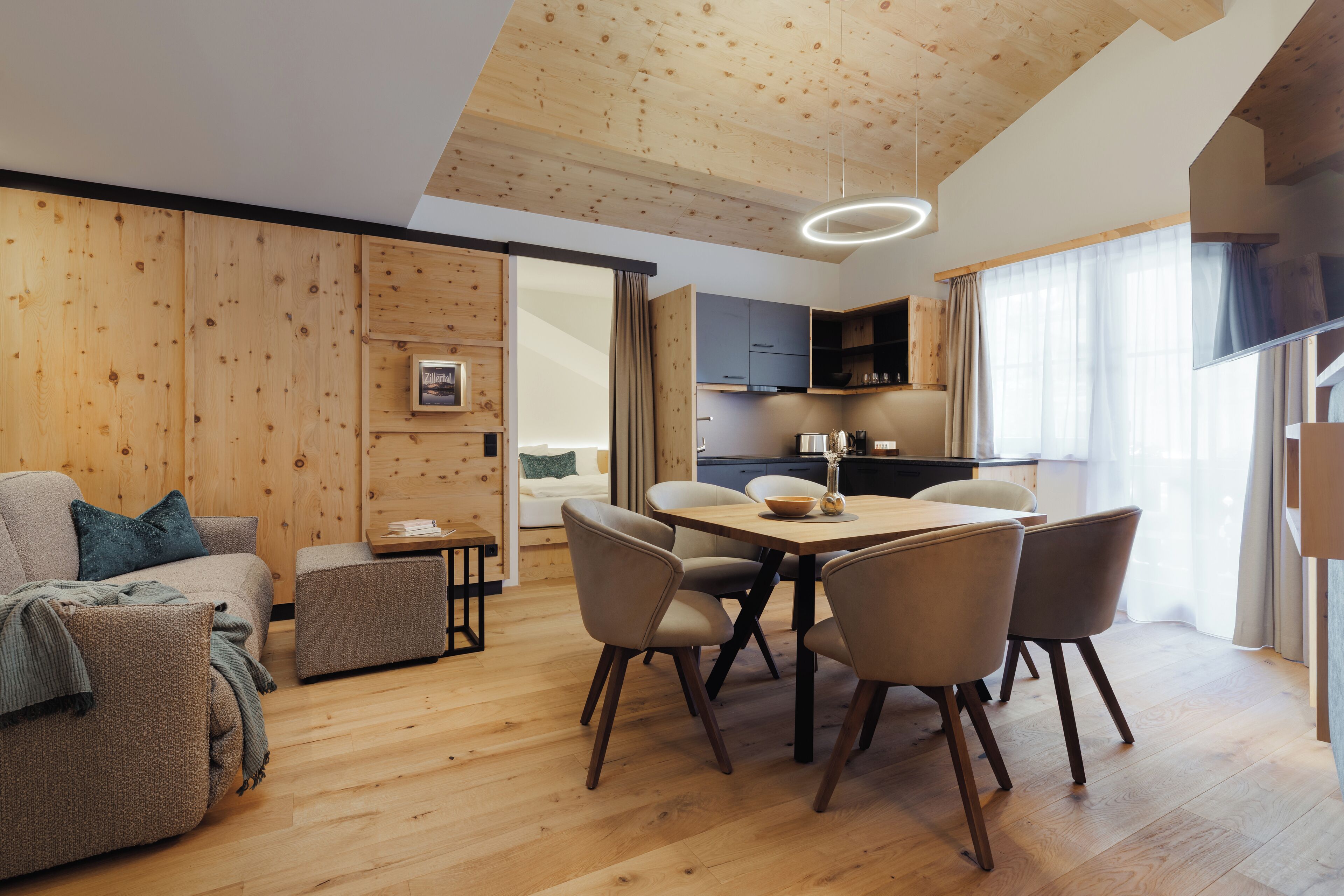 Una sala de estar moderna con techo de madera, un área de comedor con mesa y sillas, y una cocina al fondo.