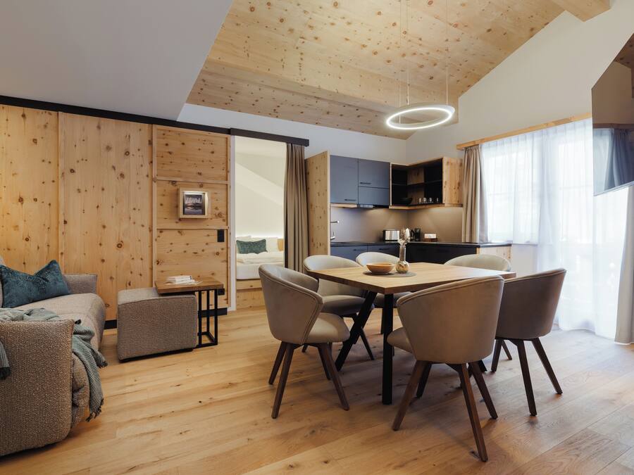 Una sala de estar moderna con techo de madera, un área de comedor con mesa y sillas, y una cocina al fondo.