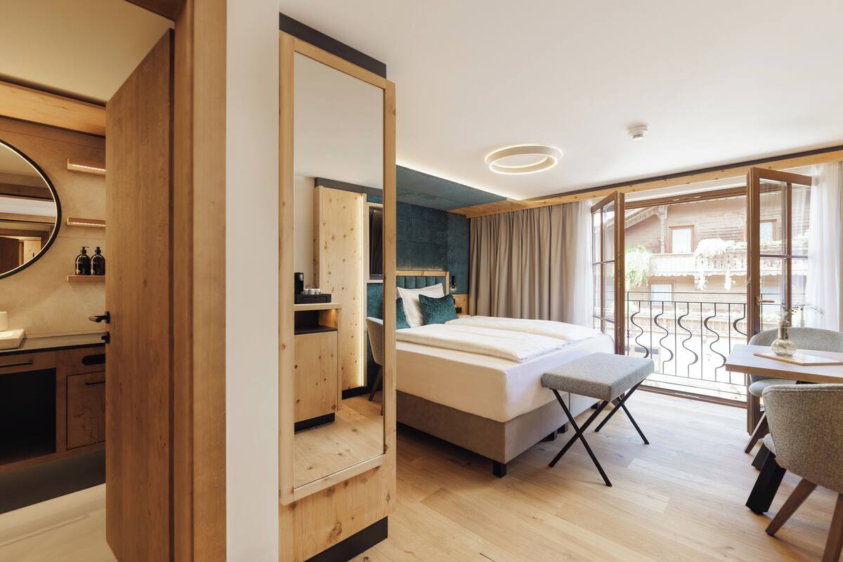 A modern hotel room with a large bed, a desk, and a balcony with a view.