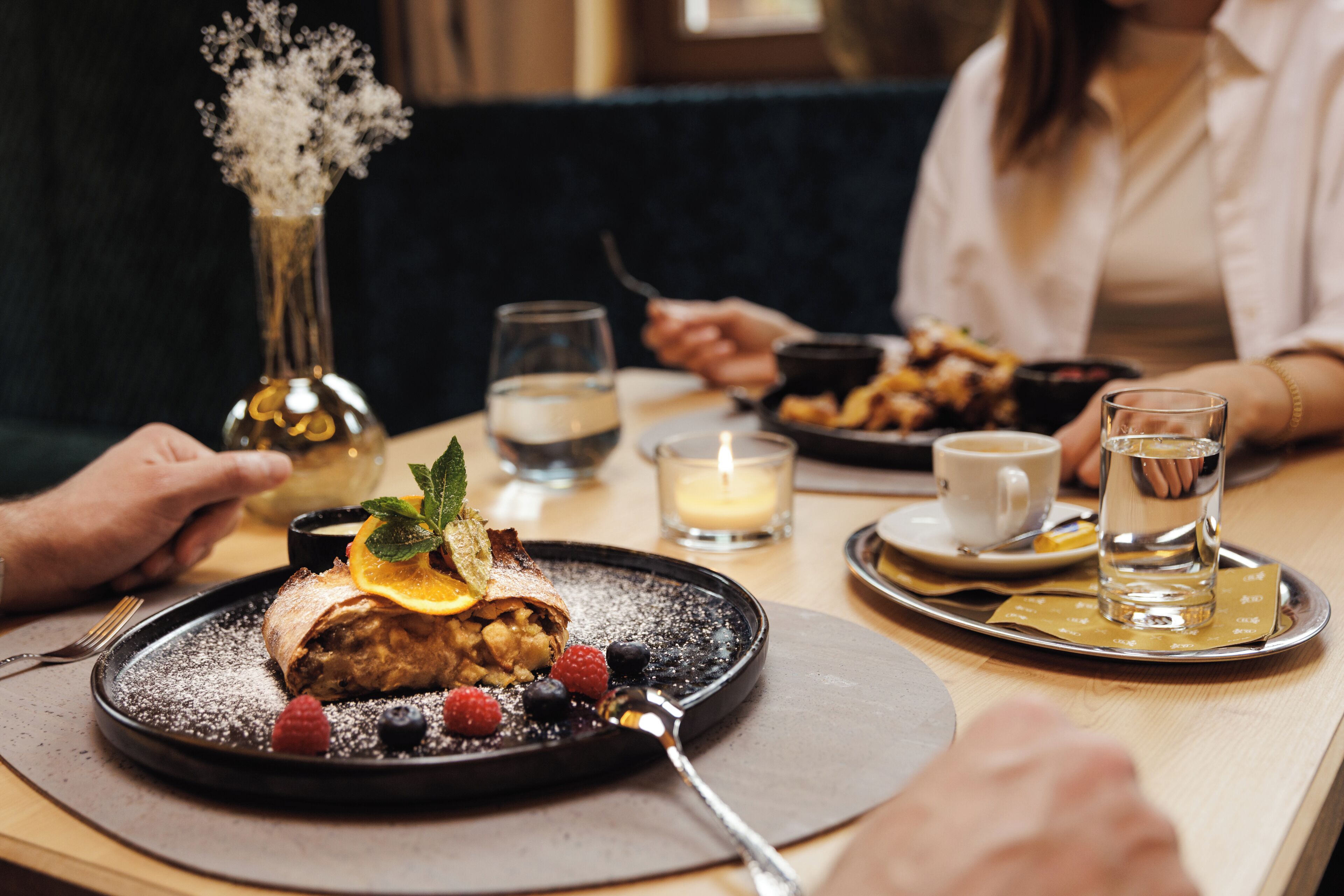 A dining table with a dessert plate, a candle, and a vase with flowers.