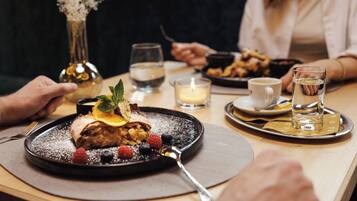 A dining table with a dessert plate, a candle, and a vase with flowers.