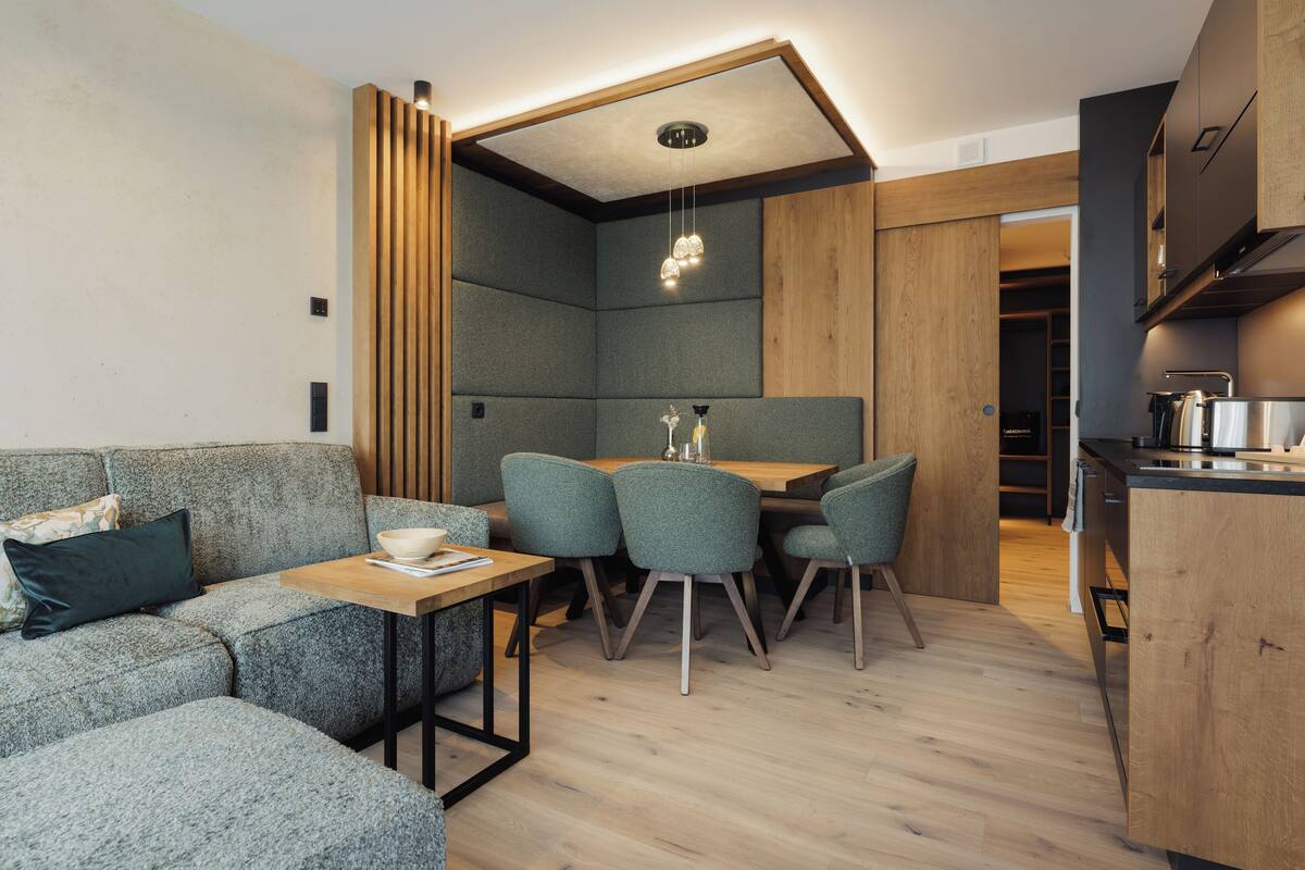 A modern kitchen with wooden cabinets, a dining area with a table and chairs, and a built-in seating area with a sofa and cushions.