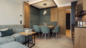Una cocina moderna con armarios de madera, un comedor con mesa y sillas, y una zona de estar integrada con sofá y cojines.