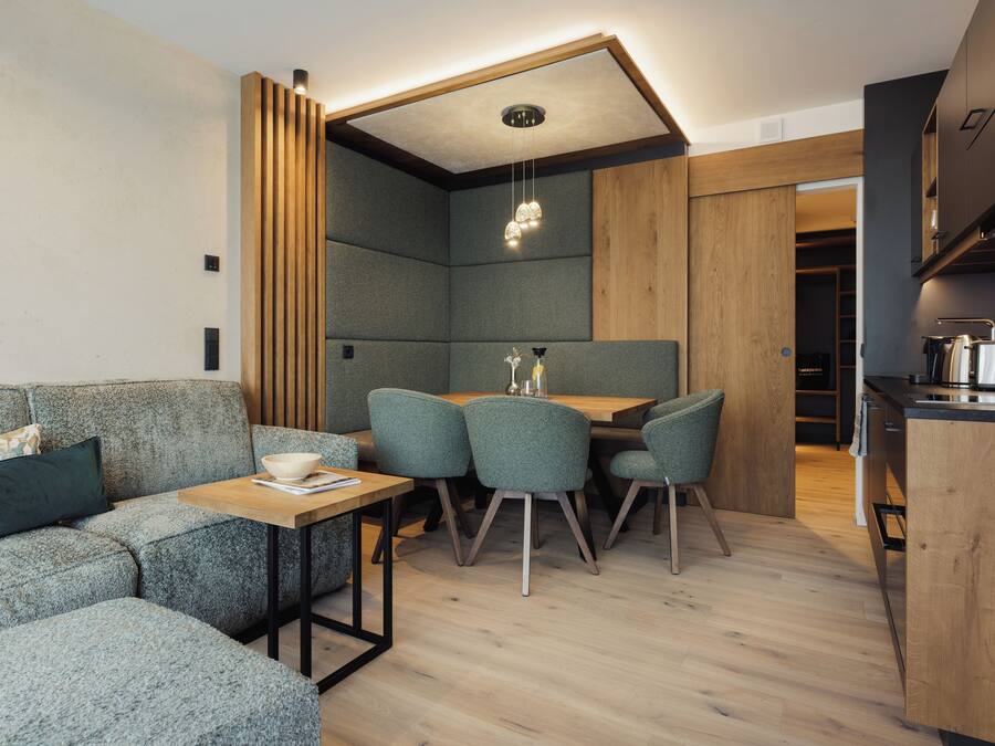 Una cocina moderna con armarios de madera, un comedor con mesa y sillas, y una zona de estar integrada con sofá y cojines.