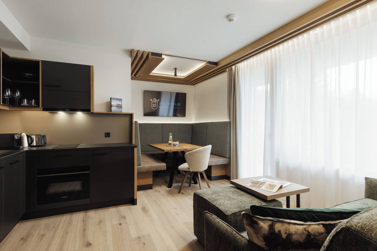 A modern kitchen with built-in appliances, a dining area with a bench, and a cozy seating area with a table and cushions.