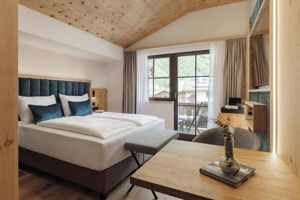 A hotel room with a large bed, a wooden table, and a view of the outdoors.