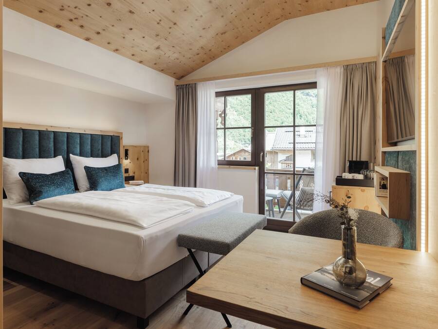 A hotel room with a large bed, a wooden table, and a view of the outdoors.