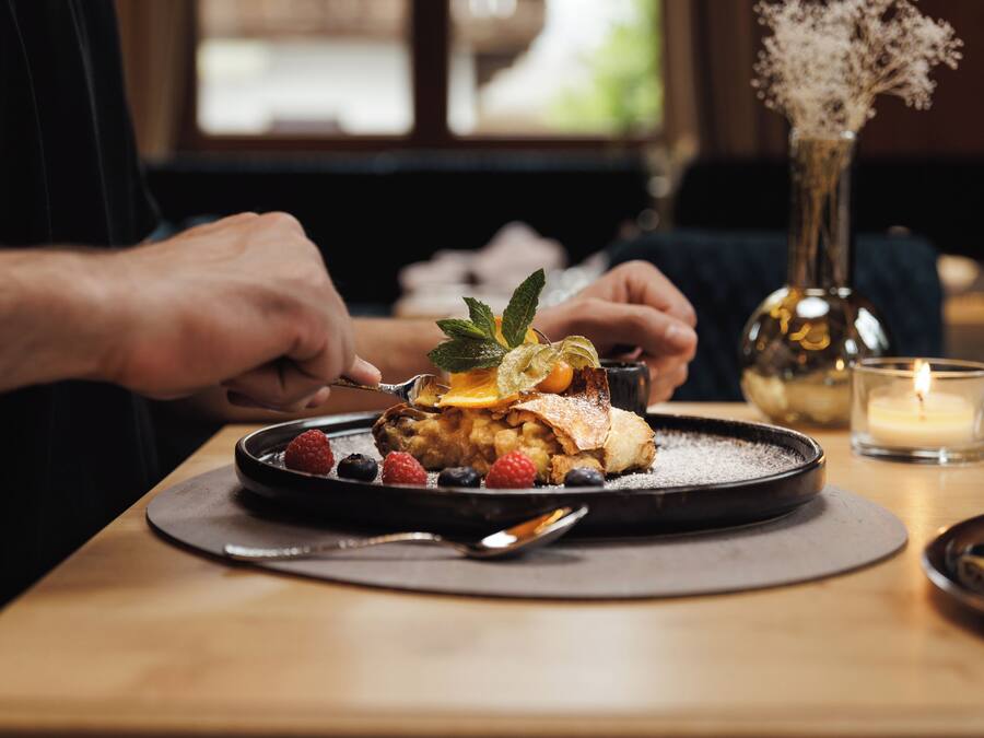 A dessert with fruit and mint on a plate, a candle, and a vase with dried flowers on a table.